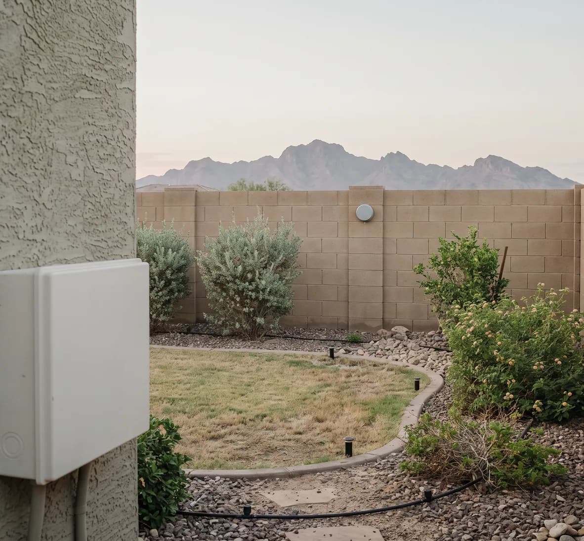 Backyard with a small weather sensor on the block wall and a closed white controller on the house wall